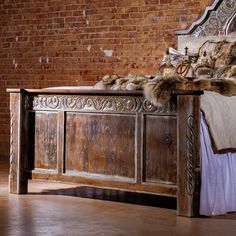 an old wooden bed with fur on the headboard and foot board, in front of a brick wall