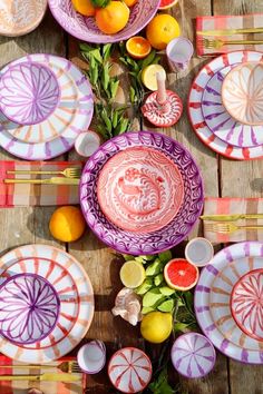 colorful plates and fruit are laid out on a wooden table with oranges, lemons, and watermelon