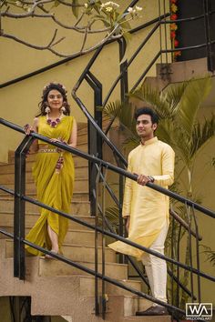 a man and woman are standing on the stairs in front of a building, dressed in yellow