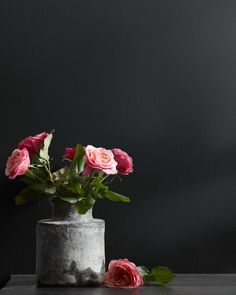 some pink roses are in a gray vase on a wooden table with dark walls behind them