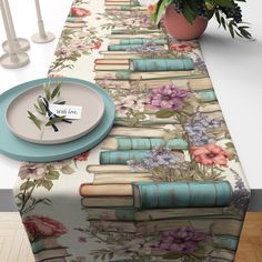 a table topped with lots of books next to a vase filled with flowers and plants