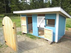 a small blue and white chicken coop next to a fenced in area with trees