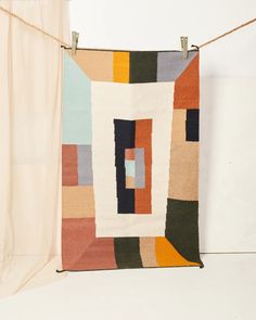 a multicolored rug hanging on a rope next to a white wall and curtain