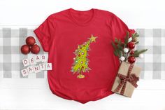 a t - shirt with a christmas tree on it next to some presents and ornaments