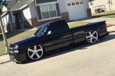 a black truck parked in front of a house on the side of the road with white rims