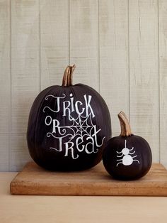 two black pumpkins sitting on top of a wooden table next to an open book