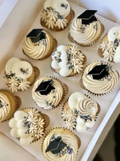 cupcakes decorated with white frosting and black graduation caps in a cardboard box