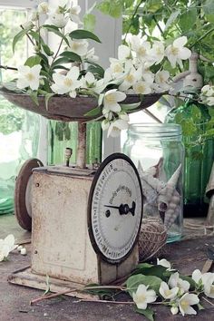 an old clock sitting on top of a table with white flowers in vases behind it