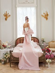 a woman in a pink dress is standing on a bed with flowers and candles around her