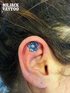 a close up of a person's ear with a blue flower tattoo on it