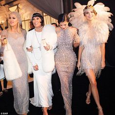 three women dressed in white and wearing feathered dresses walk down the runway at a fashion show