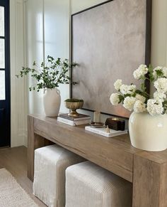 a wooden table topped with white vases filled with flowers next to a wall mounted mirror