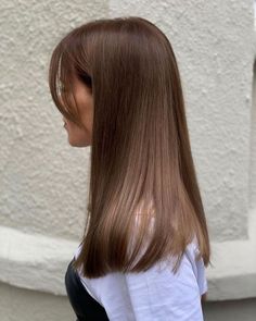 a woman with long, straight hair standing in front of a white wall and looking off to the side