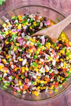 a glass bowl filled with black beans, corn and cilantros next to a wooden spoon