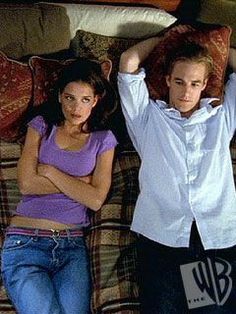 two young people laying on a couch with pillows and blankets over their heads, one holding his arms behind his head