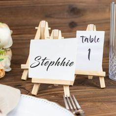 a table setting with place cards and silverware on wooden boards, along with flowers