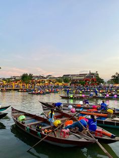 there are many small boats in the water with people on them and some buildings behind them