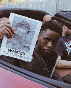 a man sitting in the back seat of a red car holding up a wanted poster