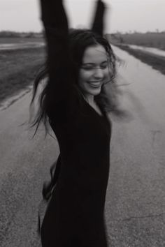 a woman with her arms up in the air on an empty road, smiling and waving