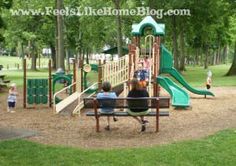 two people sitting on a bench in front of a playground with a slide and climbing frame