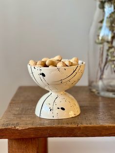 a white bowl filled with nuts sitting on top of a wooden table next to a vase