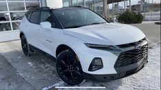 a white chevrolet suv parked in front of a building on a snow covered street with lots of windows