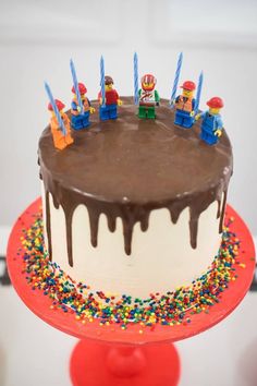 a birthday cake with chocolate icing and sprinkles on top, sitting on a red stand