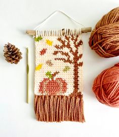 two balls of yarn and some knitting needles on a white surface with an autumn themed wall hanging