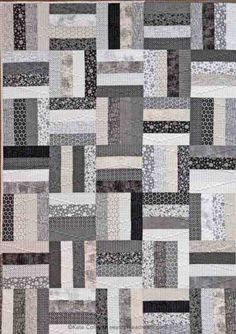 a quilt made with squares in grey and white colors on a wooden surface, the pattern is