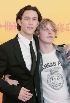 two young men standing next to each other in front of a yellow wall with words on it