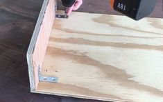 a person using a drill to attach the side of a piece of plywood