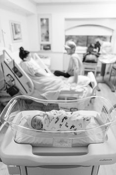 a baby laying in a hospital bed next to an adult sitting on a couch and another person standing behind it