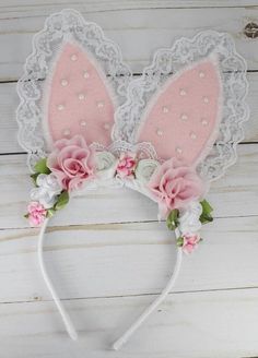 a pink bunny ears headband with flowers and lace around it on a white wooden background