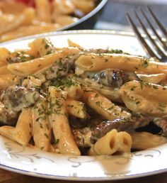 a white plate topped with pasta covered in sauce and mushrooms next to a silver fork