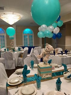 a teddy bear sitting on top of a cake surrounded by blue and white balloons in a banquet room