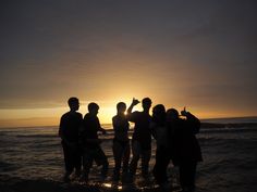 a group of people standing in the ocean at sunset