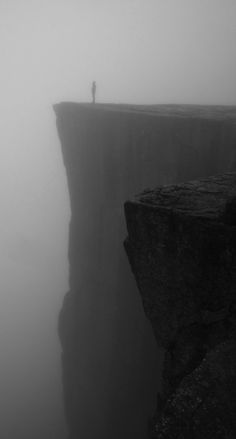 a person standing on top of a cliff in the middle of foggy weather,