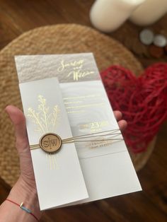 a person holding up a white and gold wedding card with a wax stamp on it