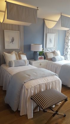 two beds in a room with blue walls and white bedding, one has a black and white striped footstool