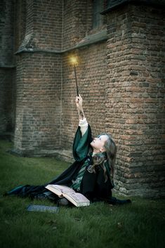 a woman sitting on the ground holding a wand in her hand and reading a book