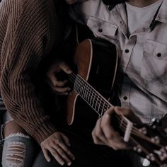 a man and woman sitting next to each other while playing the same guitar, both holding their heads together