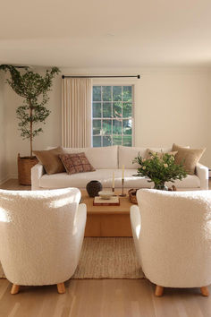 a living room with two white chairs and a coffee table in front of a window