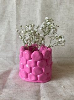 a pink vase filled with white flowers on top of a bed of cloth covered fabric