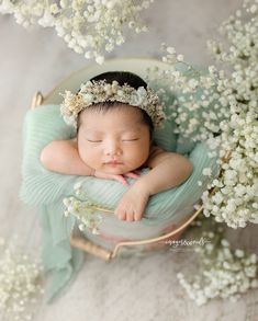 a baby is sleeping in a basket with white flowers on the side and it's head resting on its hands