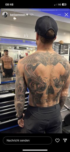 a man with tattoos on his back looking at another man in the mirror behind him