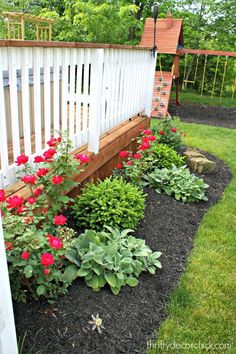 a garden with flowers and plants growing in the ground next to a white picket fence