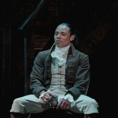 a man sitting on top of a chair wearing a suit and bow tie in a dark room