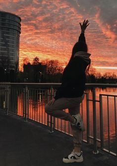 a person standing on one leg in front of a body of water with the sun setting behind them