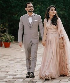 a man and woman in formal wear walking down a brick walkway holding each other's hands