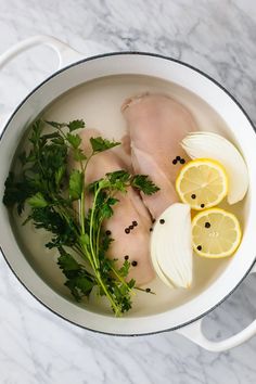 chicken, lemons and parsley in a white pot on a marble countertop